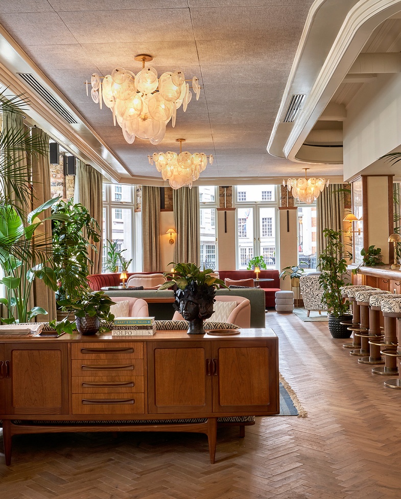 An open-plan Maslow’s members' lounge featuring mid-century furniture, lush greenery, soft lighting, and layered textures—designed for comfort, connection, and quiet luxury.