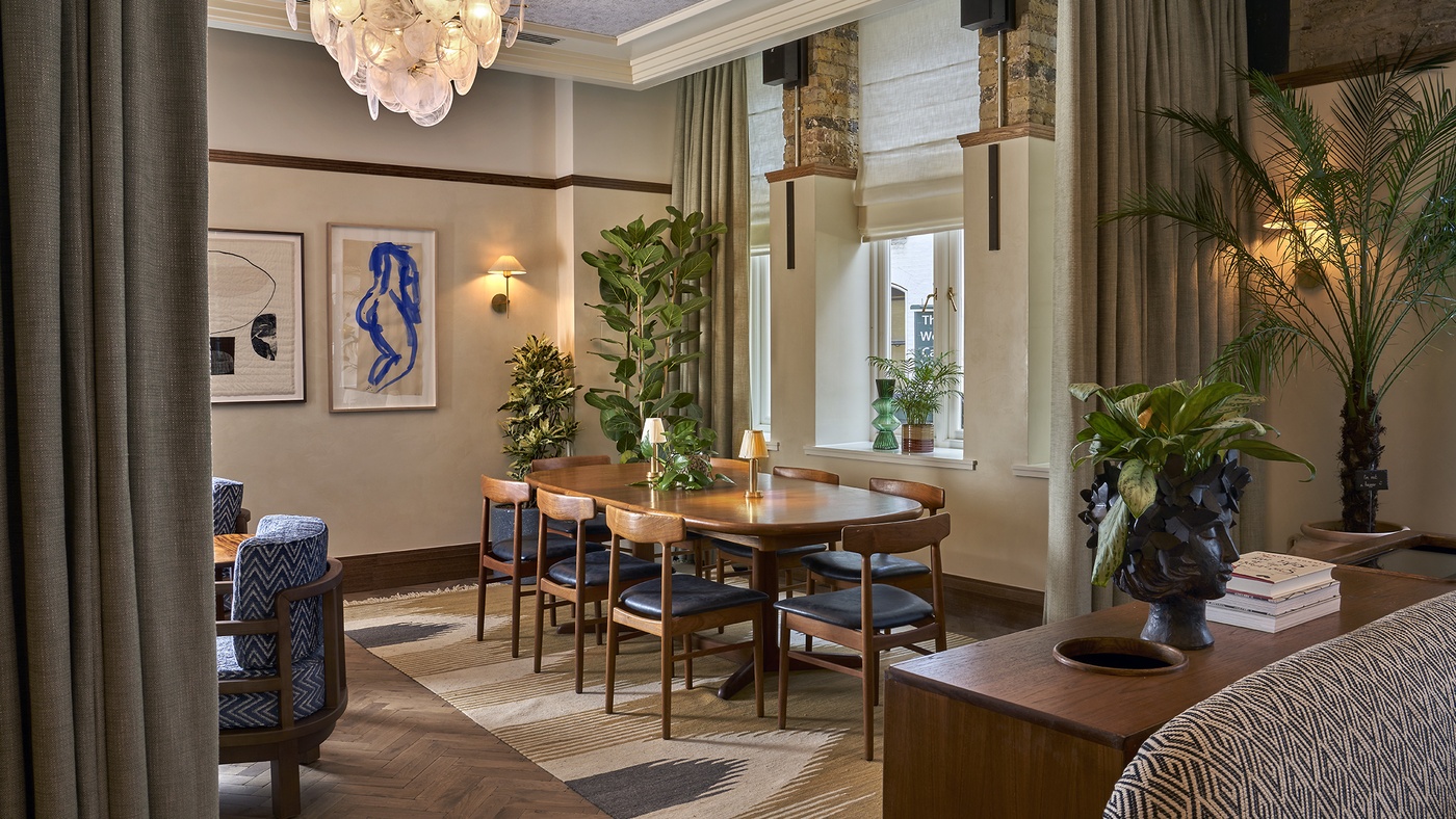Stylish private dining room at 1 Warwick in Soho, London, featuring a mid-century table, plush seating, plants, and warm lighting.