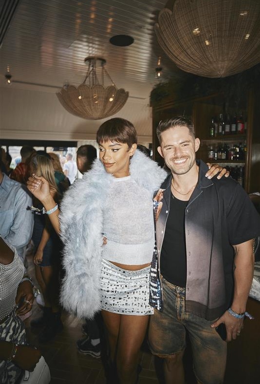 Two guests posing together and smiling during a lively private event in London, with a bar and chandeliers in the background.