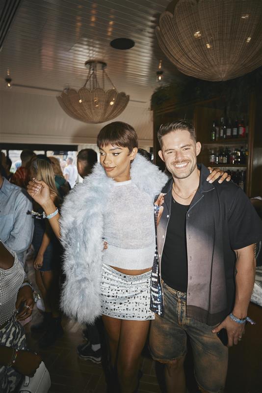 Two guests posing together and smiling during a lively private event in London, with a bar and chandeliers in the background.