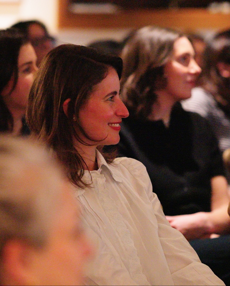 Smiling woman in a white blouse seated among an attentive audience during a private event in London.