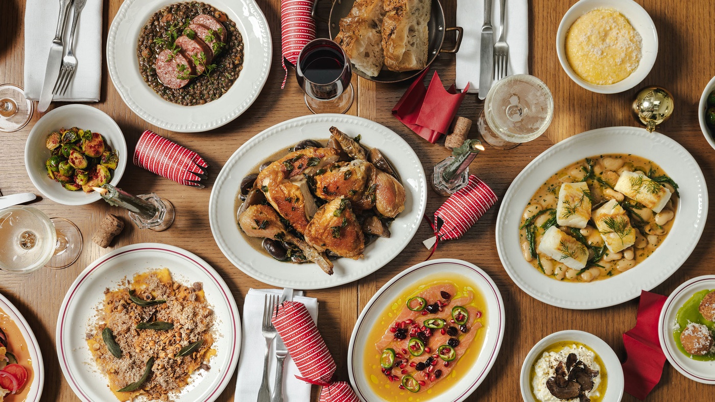 Overhead view of a festive sharing feast at Maslow’s Mortimer House in London, featuring roast chicken, seasonal vegetables, pasta, fish, and Christmas crackers.