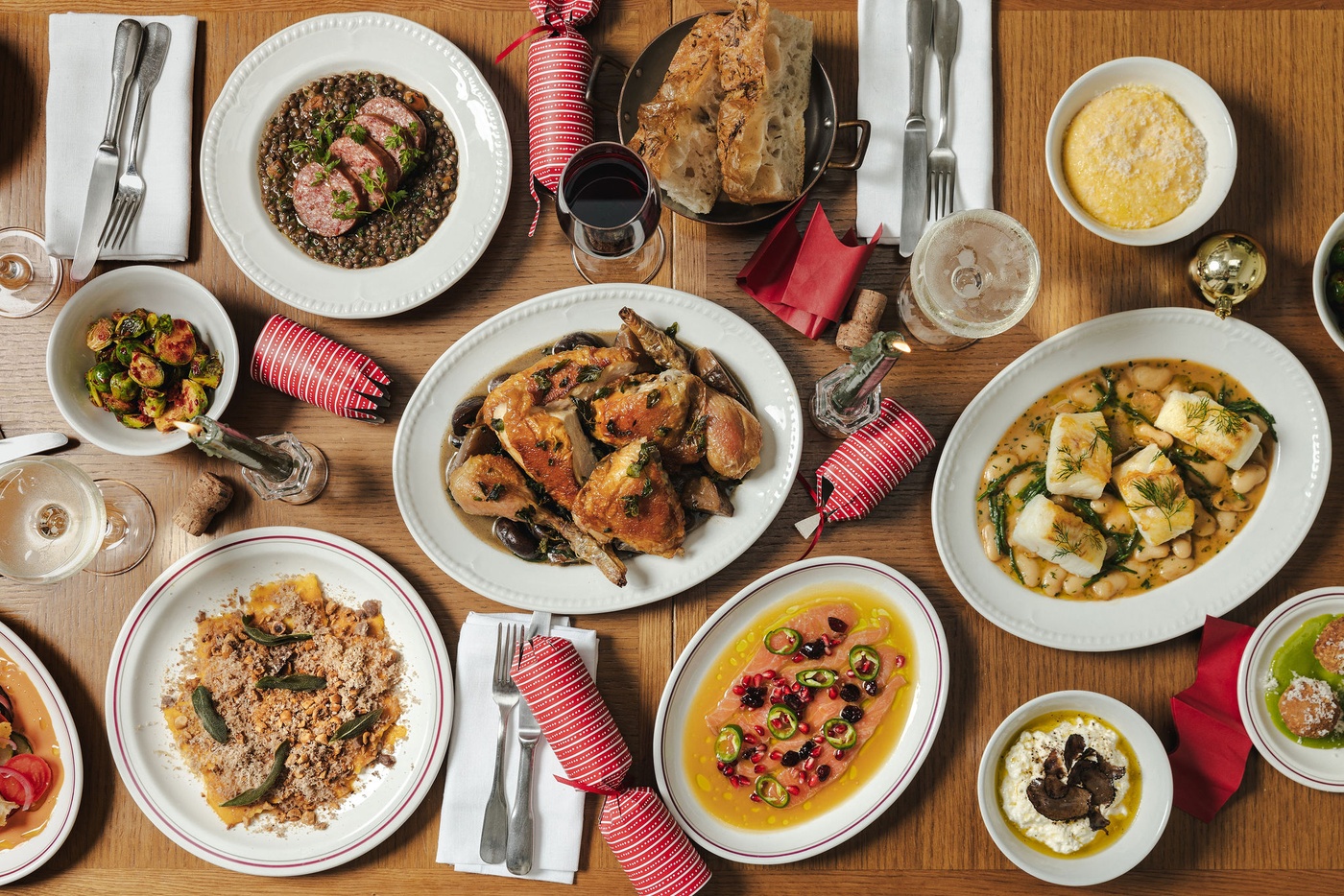 Overhead view of a festive sharing feast at Maslow’s Mortimer House in London, featuring roast chicken, seasonal vegetables, pasta, fish, and Christmas crackers.