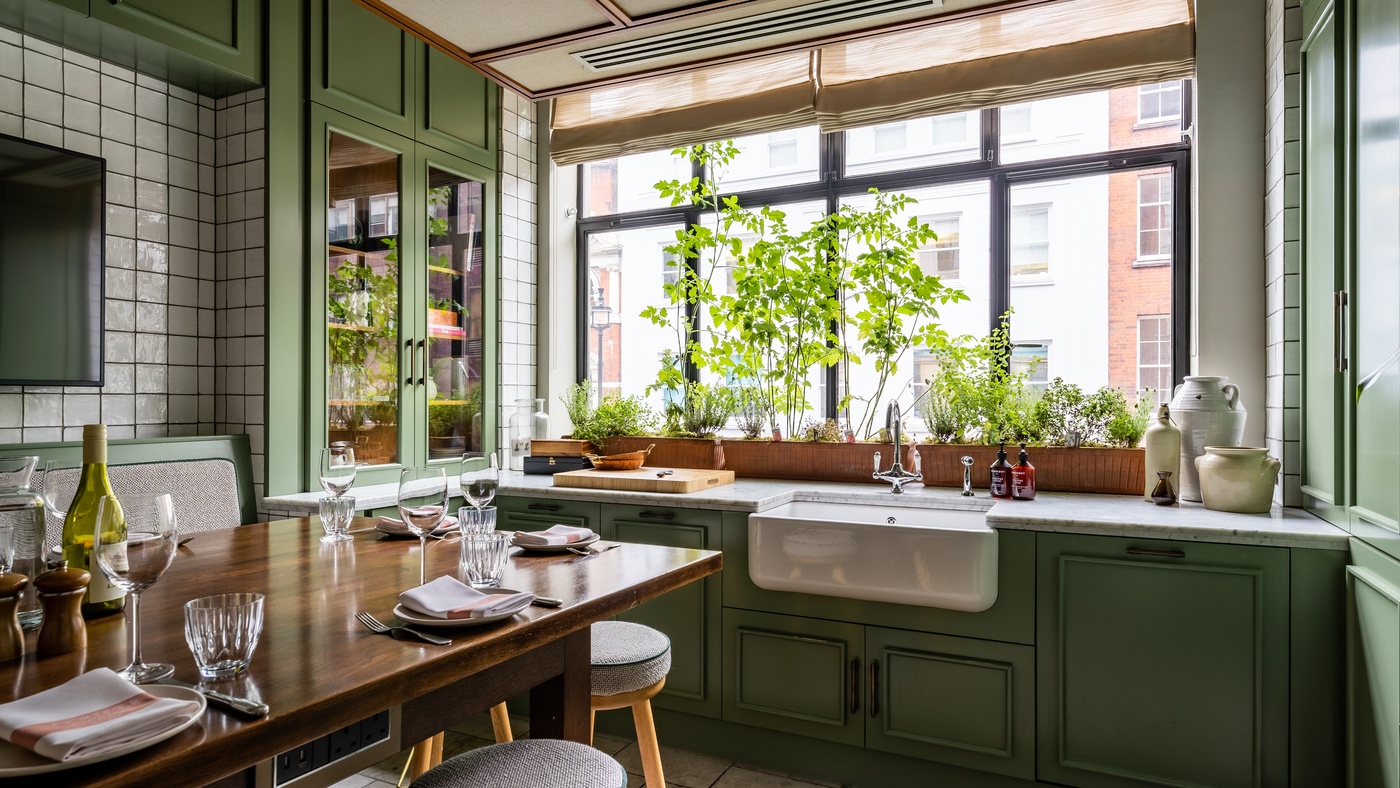 Bright and homely Kitchen Table private dining space at Mortimer House in London, with green cabinetry, farmhouse sink, and set dining table.