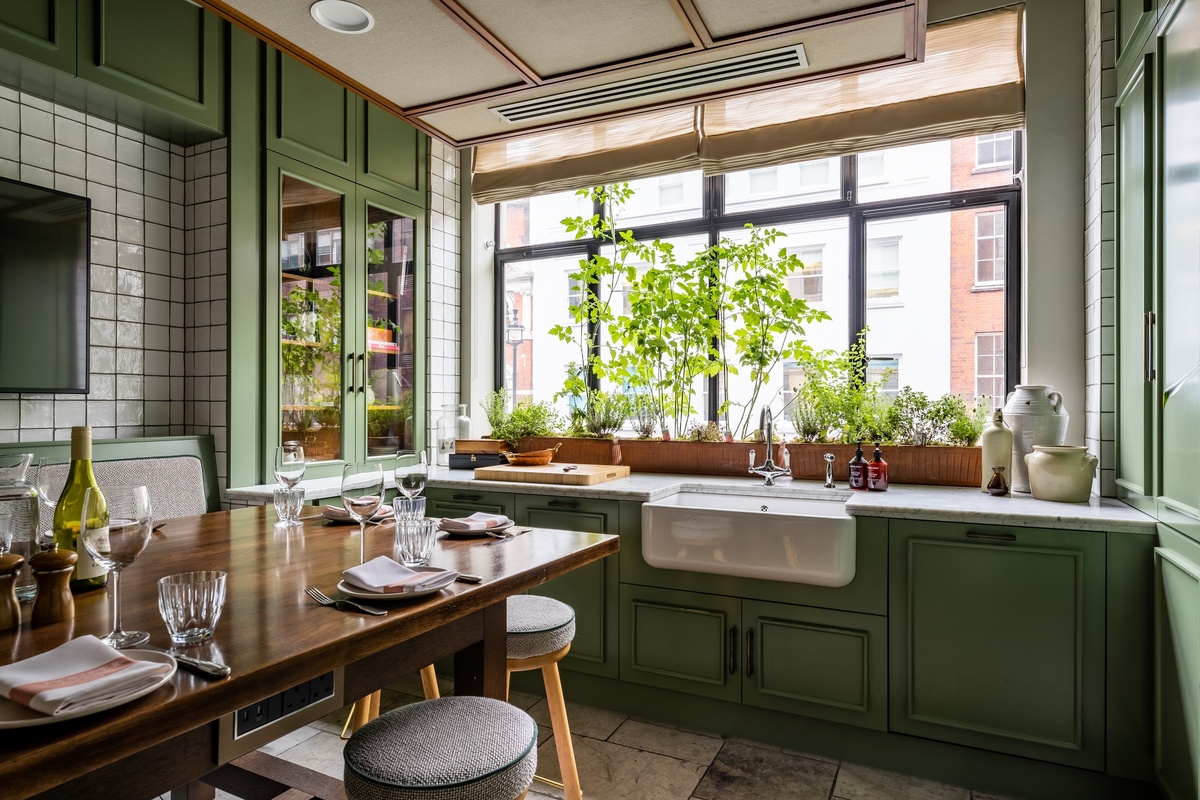 Bright and homely Kitchen Table private dining space at Mortimer House in London, with green cabinetry, farmhouse sink, and set dining table.