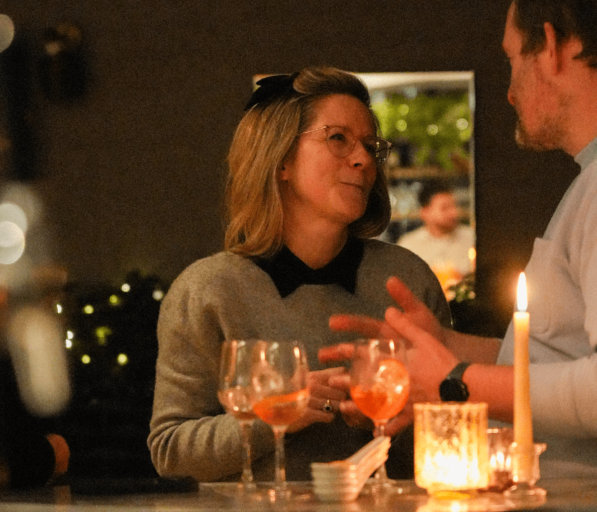 Two people enjoying festive cocktails by candlelight at Maslow’s in London, sharing conversation in a warm, intimate setting.