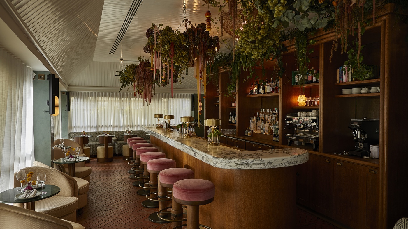 Yasmin rooftop bar at 1 Warwick in Soho, London, featuring marble counter, pink velvet stools, hanging foliage, and soft natural light.