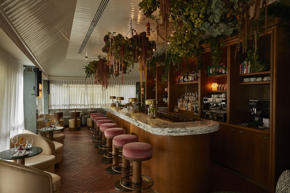 Yasmin rooftop bar at 1 Warwick in Soho, London, featuring marble counter, pink velvet stools, hanging foliage, and soft natural light.